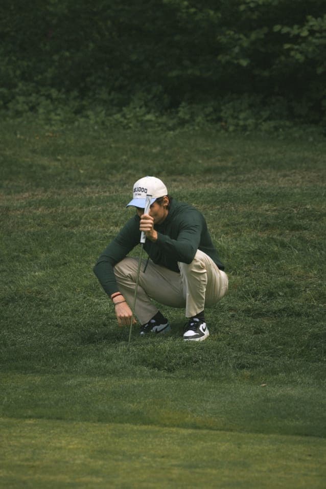 Player in a Dogleg cap crouching to read the slope of a green