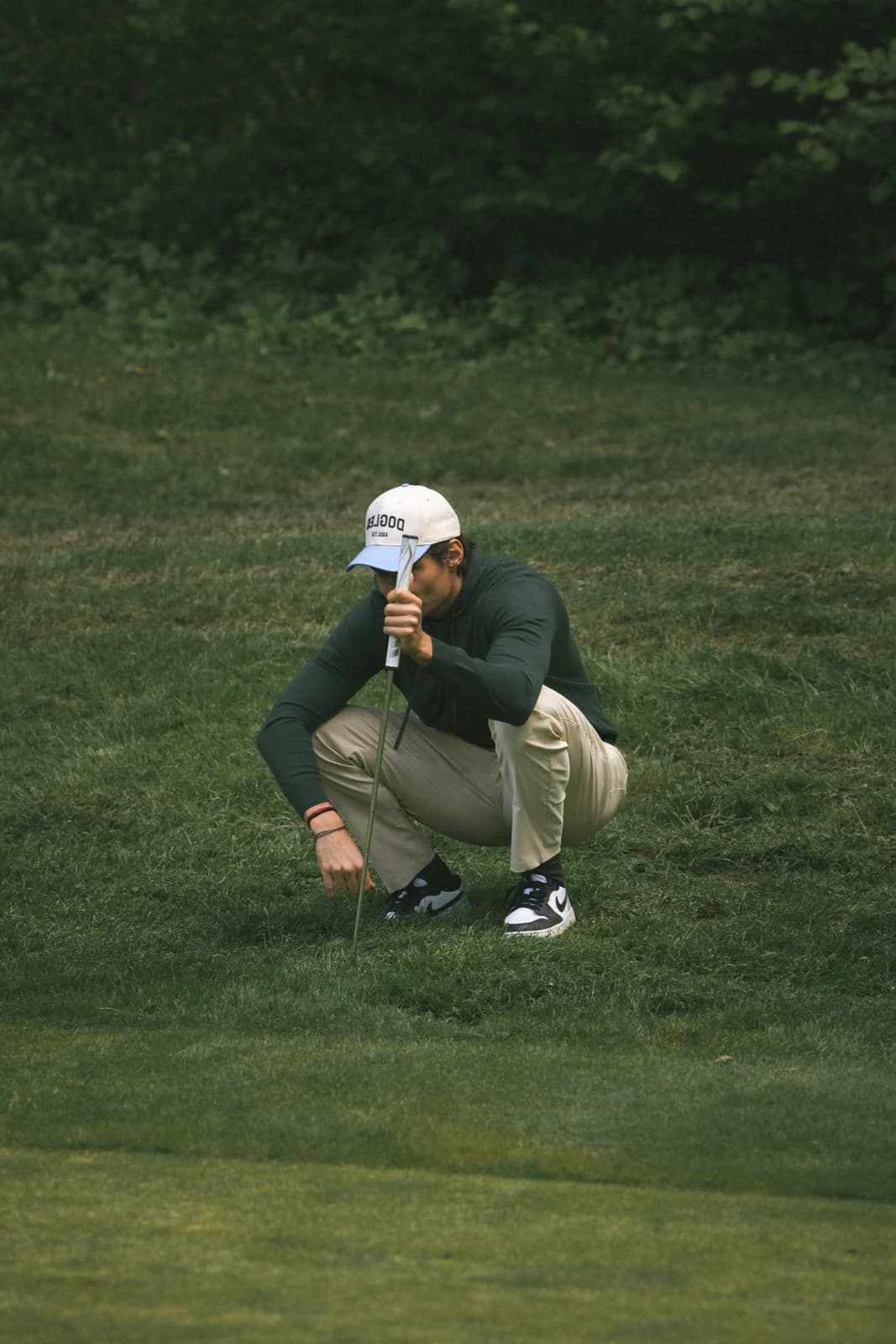 Golfer crouched on the green in beige trousers