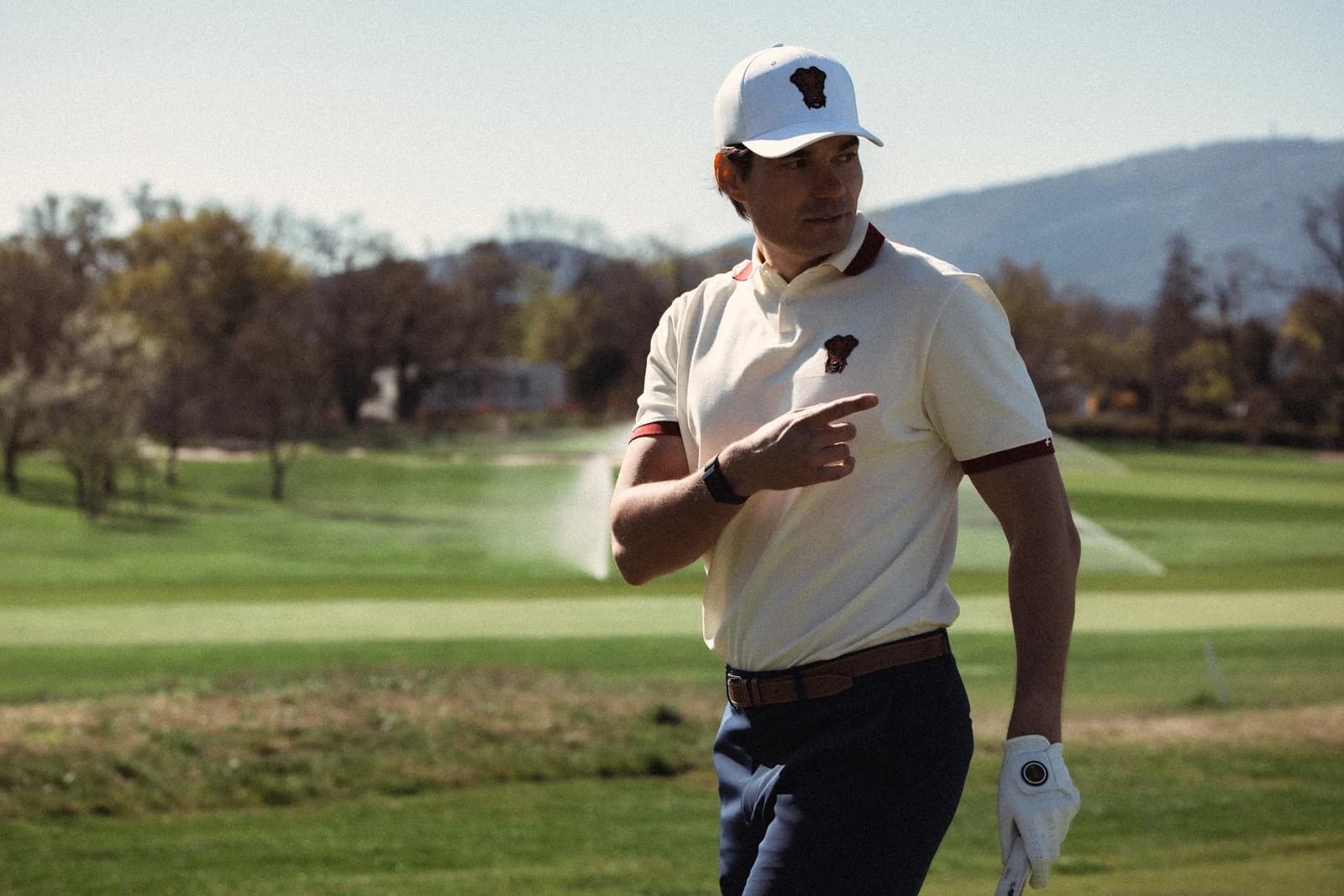 Golfer in a cream polo, arm raised across the chest